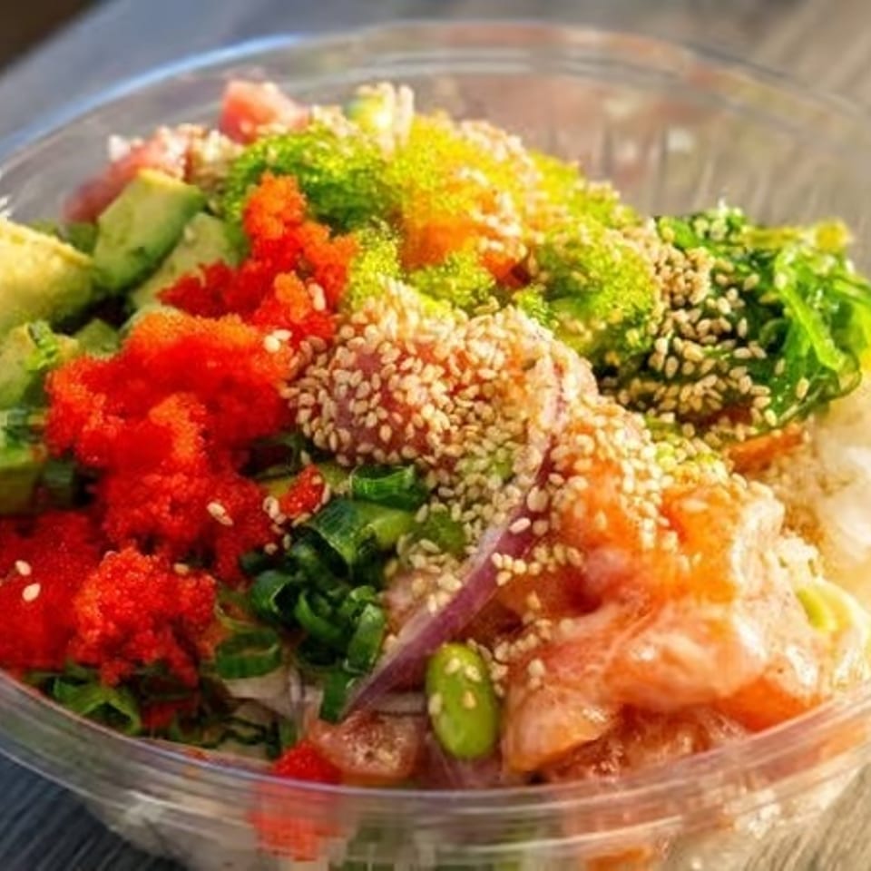 Colorful poke bowl with salmon, tuna, avocado, roe, seaweed, and sesame seeds.