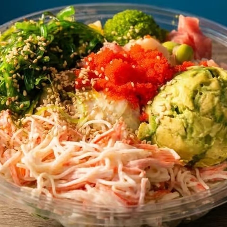 A colorful poke bowl with avocado, crab, seaweed salad, and roe in a clear plastic container.