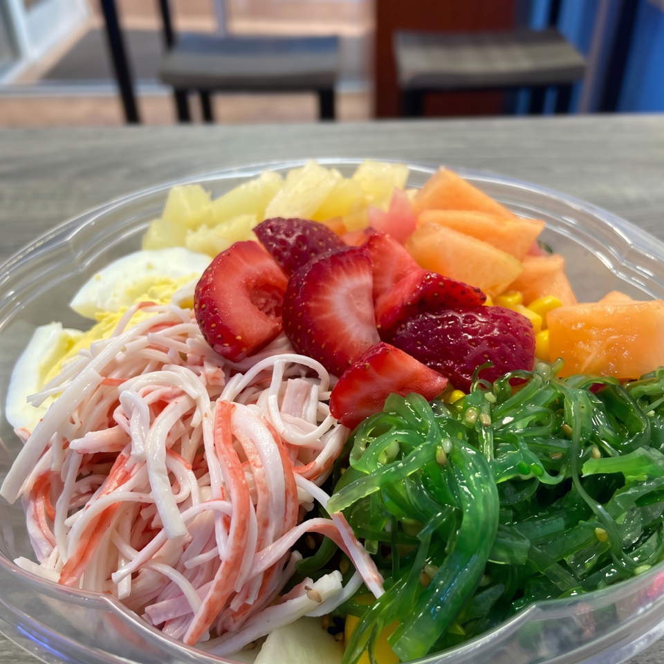 A colorful poke bowl with crab sticks, seaweed, strawberries, pineapple, cantaloupe, and hard-boiled egg.