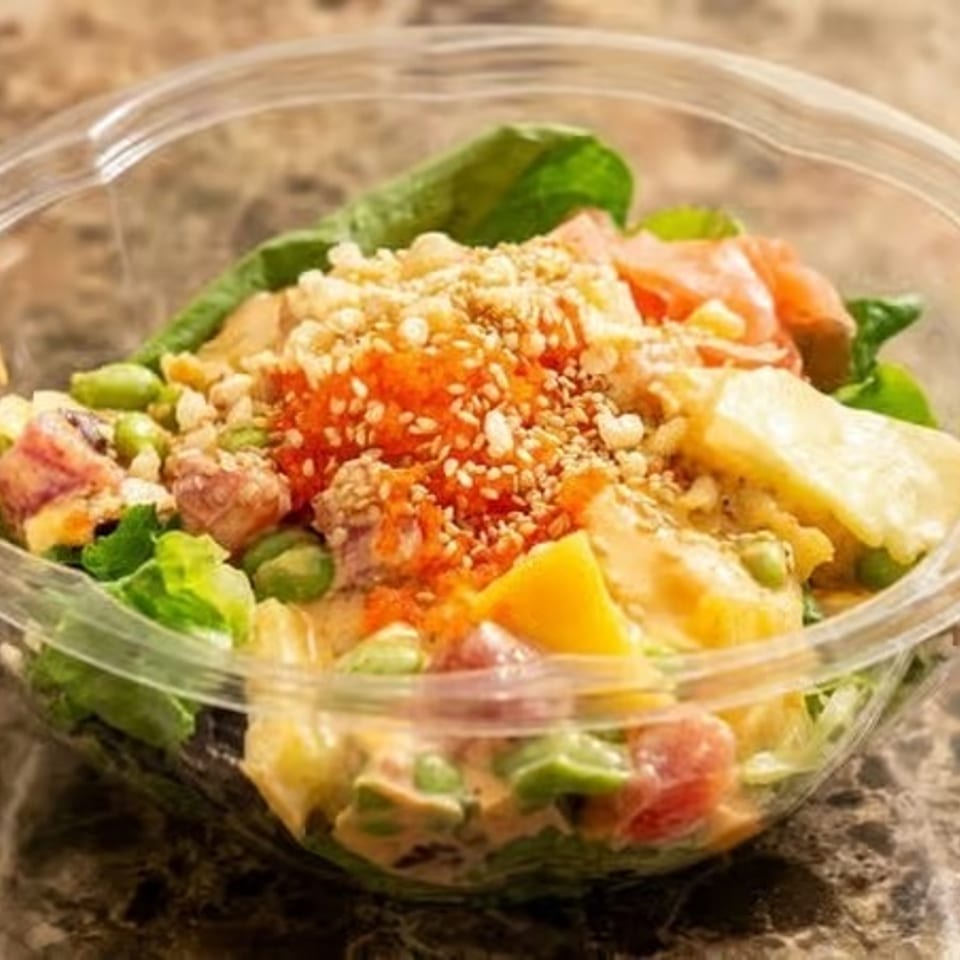 Colorful poke bowl with salmon, tuna, mango, edamame, and roe in a clear plastic container.