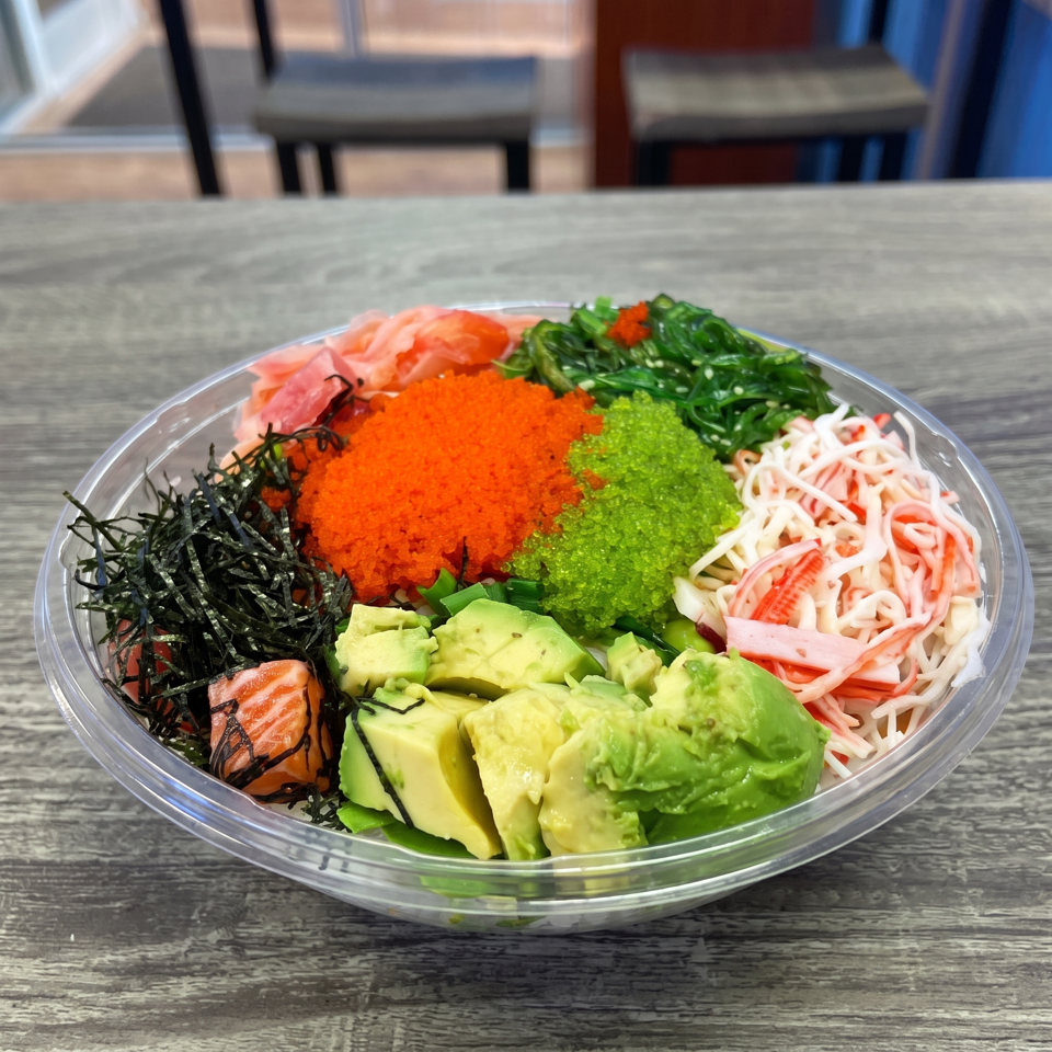 Colorful poke bowl with salmon, avocado, crab, seaweed, and roe on a wooden table.