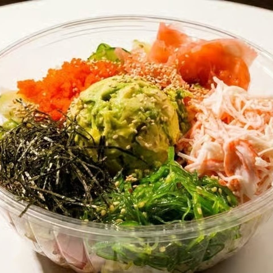 Colorful poke bowl with avocado, salmon, crab, seaweed, and roe in a clear plastic container.