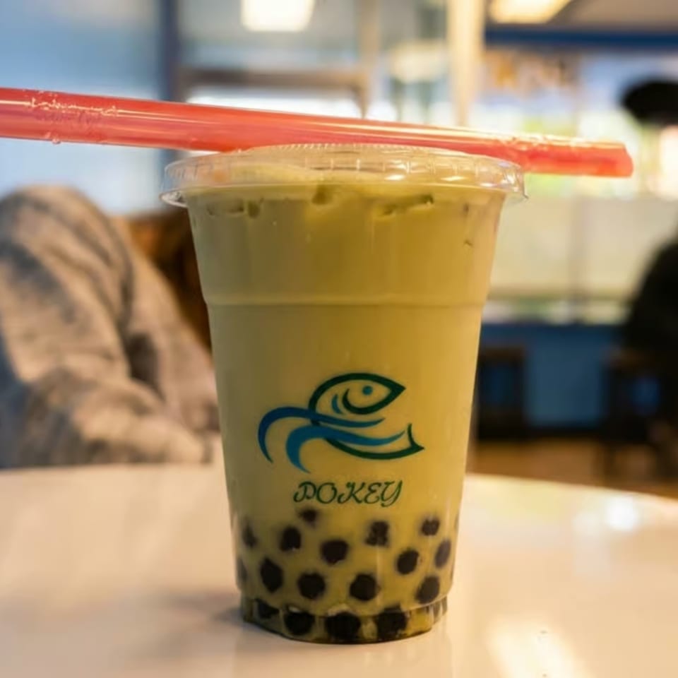 A green Pokey bubble tea with tapioca pearls and a red straw on a white table.