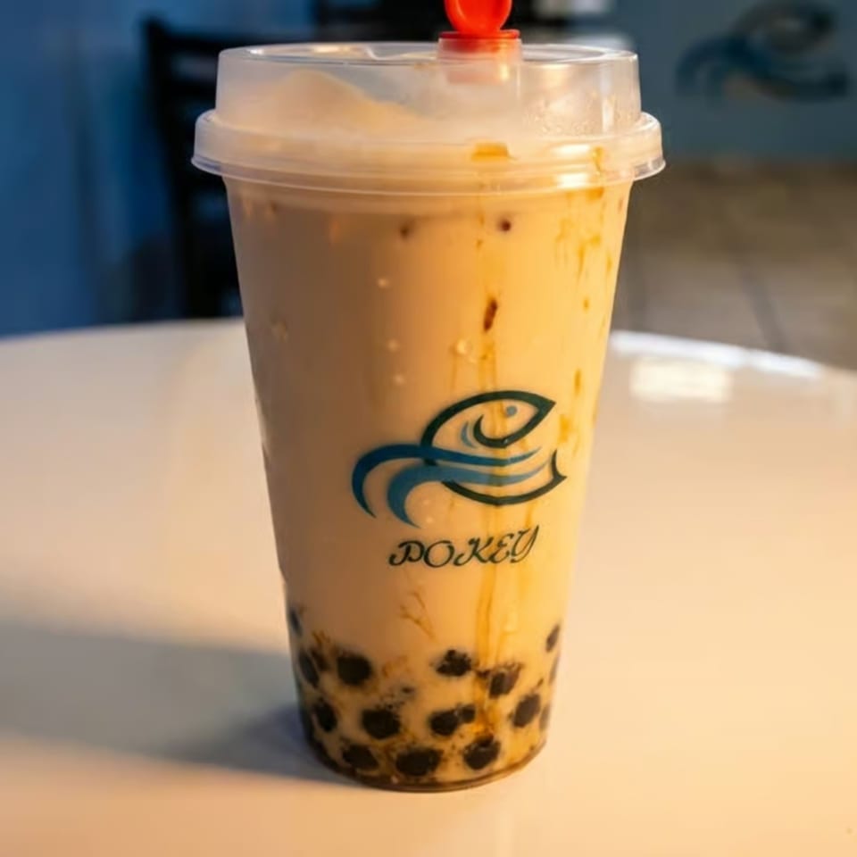A large plastic cup of Pokey bubble tea with tapioca pearls on a white table.